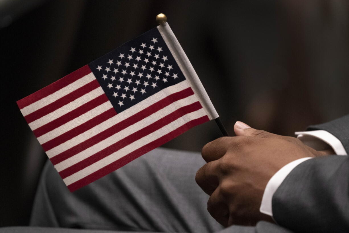 FILE - Leon Small, originally from Jamaica, holds a United States flag in a naturalization ceremony, Wednesday, April 28, 2021, in New York. While on the brink of furloughing 70% of its roughly 20,000 employees that summer, U.S. Citizenship and Immigration said almost overnight that it would end the year with the large surplus.