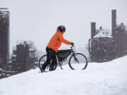 Noah Neighbor pushes his mountain bike up Kite Hill in the snow at Gas Works Park Sunday, Dec. 26, 2021, in Seattle. Snow is blanketing parts of the Pacific Northwest because of unusually cold temperatures.  Seattle got between 3 and 5 inches of snow as of Sunday morning.