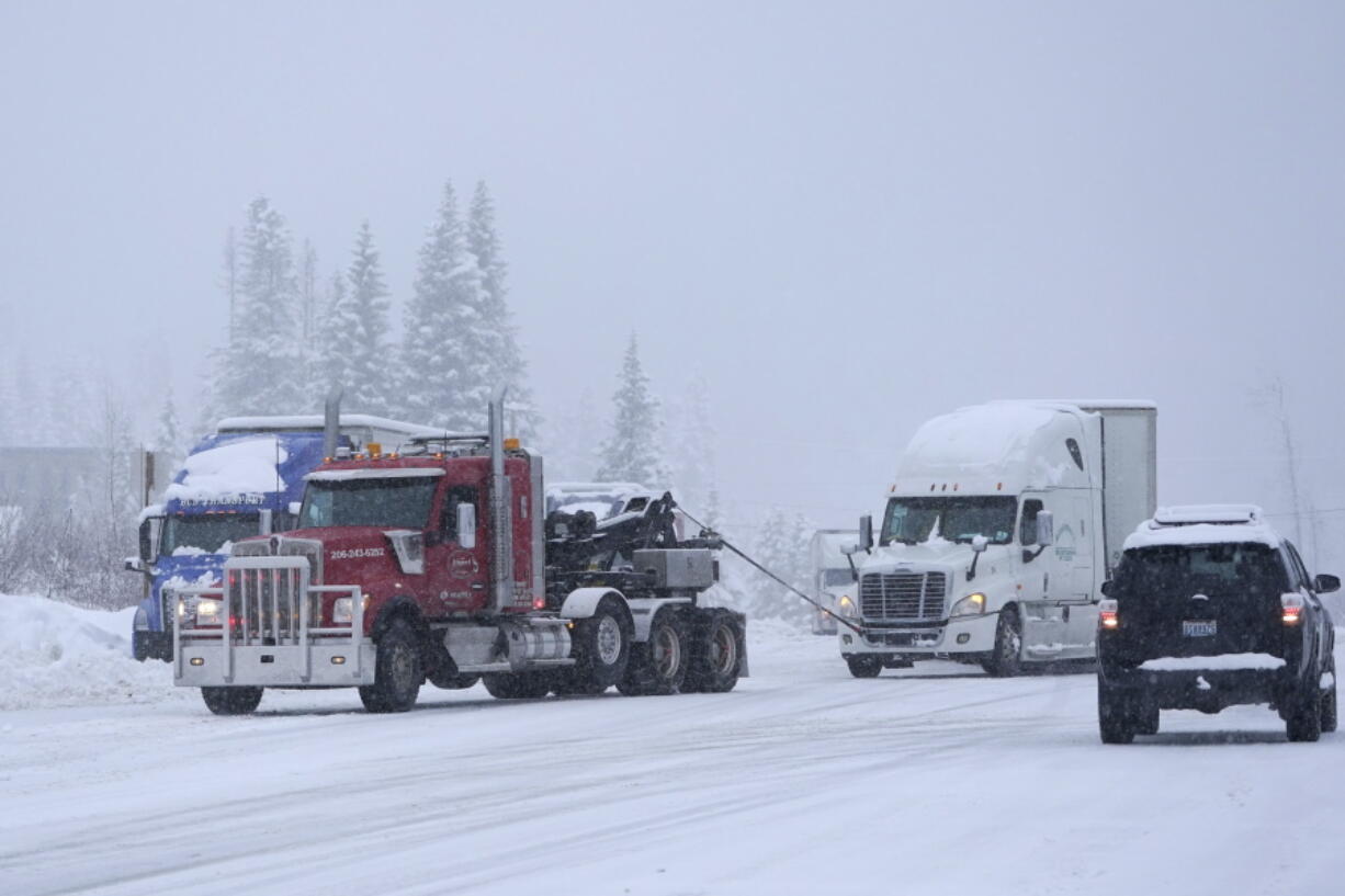 A semi-truck that was stuck in snow on the side of a road is towed out near the Summit at Snoqualmie Ski Area, Thursday, Dec. 9, 2021, at Snoqualmie Pass in Washington state. Heavy snowfall Thursday slowed traffic and led to periodic closures of Interstate Highway 90. (AP Photo/Ted S. Warren) (ted s.