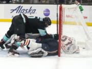 Seattle Kraken's Mark Giordano, left, tumbles atop Edmonton Oilers' Warren Foegele (37) while Kraken goalie Chris Driedger is buried below as the puck sits in the back of the net in the third period of an NHL hockey game Saturday, Dec. 18, 2021, in Seattle. The play was eventually ruled a goal by Foegele.