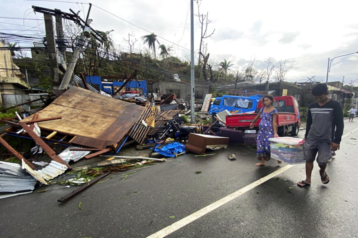 Residents carry what's left of their belongings as they walk past damaged homes due to Typhoon Rai in Surigao city, Surigao del Norte, central Philippines on Friday Dec. 17, 2021. A powerful typhoon left more than a dozen people dead, knocked down power and communications in entire provinces and wrought widespread destruction mostly in the central Philippines, officials said Saturday.