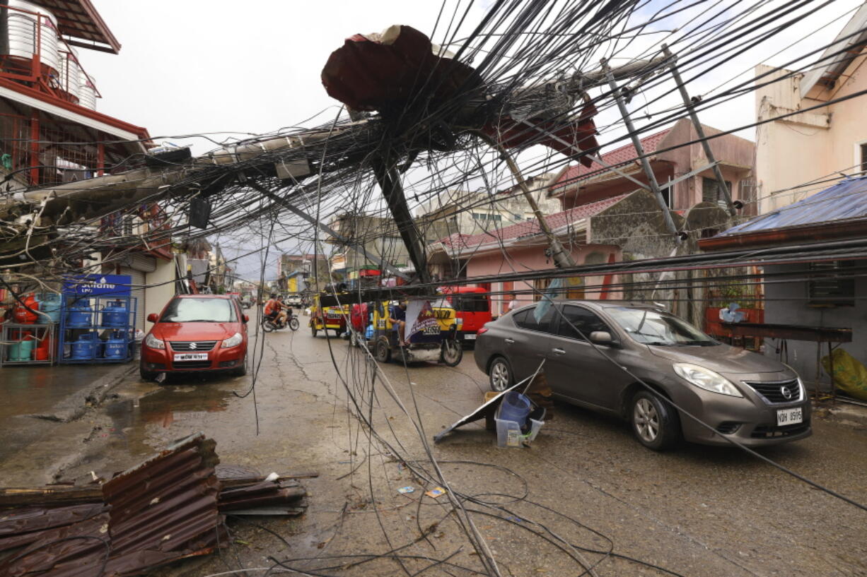 Cars pass by a toppled electrical post due to Typhoon Rai in Surigao city, Surigao del Norte, southern Philippines as power supply remain down on Sunday Dec. 19, 2021. The death toll in the strongest typhoon to batter the Philippines this year continues to rise and the governor of an island province especially hard-hit by Typhoon Rai said there may be even greater devastation that has yet to be reported.