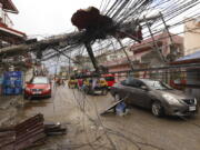 Cars pass by a toppled electrical post due to Typhoon Rai in Surigao city, Surigao del Norte, southern Philippines as power supply remain down on Sunday Dec. 19, 2021. The death toll in the strongest typhoon to batter the Philippines this year continues to rise and the governor of an island province especially hard-hit by Typhoon Rai said there may be even greater devastation that has yet to be reported.