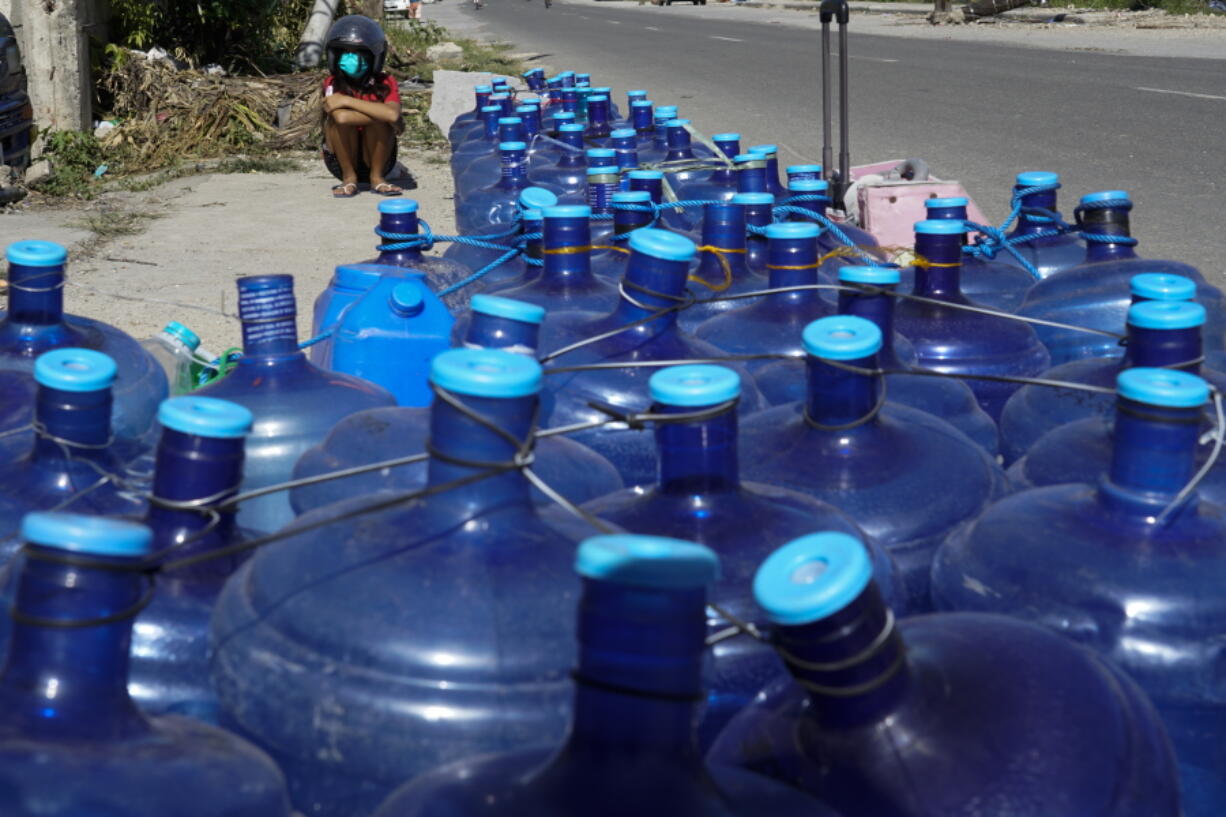 A boy sits beside water containers as residents line up for water as pipelines and electricity were damaged due to Typhoon Rai in Cebu province, central Philippines on Monday Dec. 20, 2021. The death toll in the strongest typhoon to batter the Philippines this year continues to rise and the governor of an island province especially hard-hit by Typhoon Rai said there may be even greater devastation that has yet to be reported.