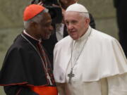 FILE  - Pope Francis talks with Cardinal Peter Kodwo Appiah Turkson during his weekly general audience, in Paul VI Hall at the Vatican, Wednesday, Jan. 15, 2020. Pope Francis on Thursday, Dec. 23, 2021 removed the head of the Vatican office that handles the high-priority issues of migration, environment and COVID-19 and put a trusted cardinal and one of the Holy See's most influential nuns at the helm instead, albeit temporarily.