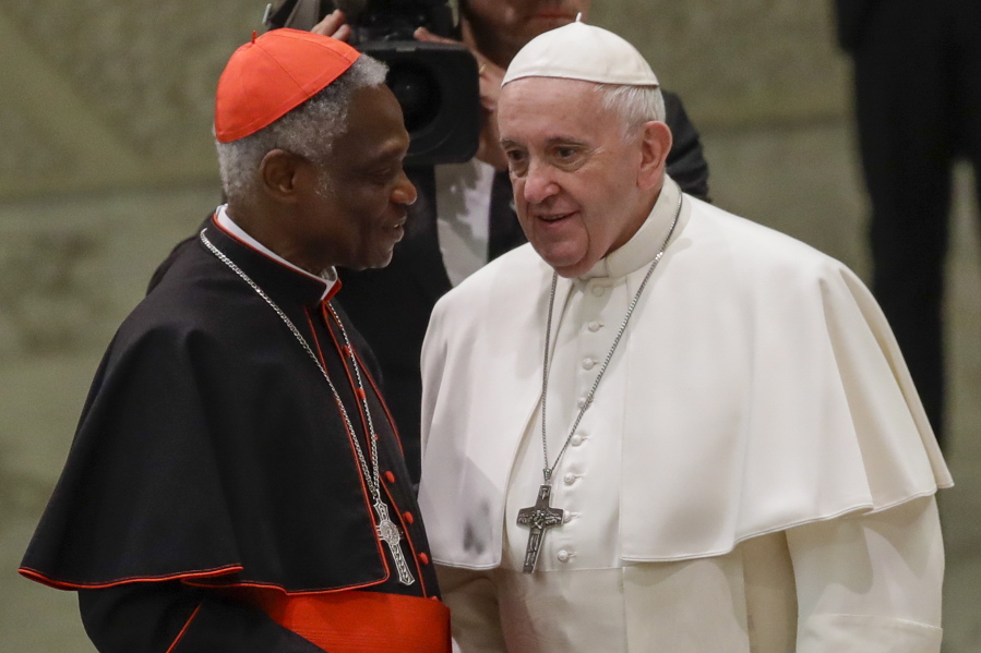 FILE  - Pope Francis talks with Cardinal Peter Kodwo Appiah Turkson during his weekly general audience, in Paul VI Hall at the Vatican, Wednesday, Jan. 15, 2020. Pope Francis on Thursday, Dec. 23, 2021 removed the head of the Vatican office that handles the high-priority issues of migration, environment and COVID-19 and put a trusted cardinal and one of the Holy See's most influential nuns at the helm instead, albeit temporarily.