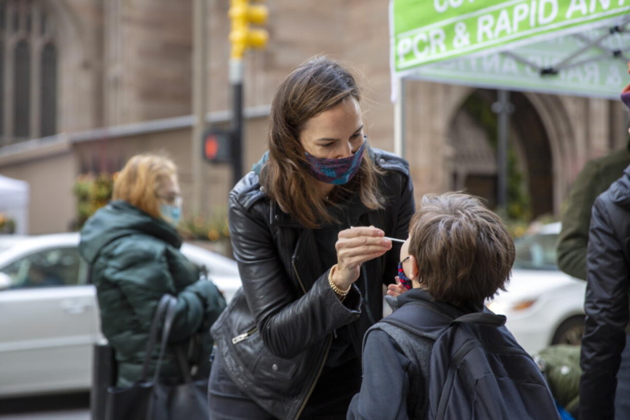 FILE - Katie Lucey administers a COVID-19 test on her son Maguire at a PCR and Rapid Antigen COVID-19 coronavirus test pop up on Wall Street in New York on Thursday, Dec. 16, 2021.   U.S. health officials are endorsing 'test-to-stay' policies that will allow close contacts of infected students to remain in classrooms. The Centers for Disease Control and Prevention on Friday, Dec. 17,  decided to more firmly embrace the approach, after research of such policies in the Chicago and Los Angeles areas found COVID-19 infections did not increase when schools switched to test-to-stay.