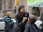 FILE - Katie Lucey administers a COVID-19 test on her son Maguire at a PCR and Rapid Antigen COVID-19 coronavirus test pop up on Wall Street in New York on Thursday, Dec. 16, 2021.   U.S. health officials are endorsing 'test-to-stay' policies that will allow close contacts of infected students to remain in classrooms. The Centers for Disease Control and Prevention on Friday, Dec. 17,  decided to more firmly embrace the approach, after research of such policies in the Chicago and Los Angeles areas found COVID-19 infections did not increase when schools switched to test-to-stay.