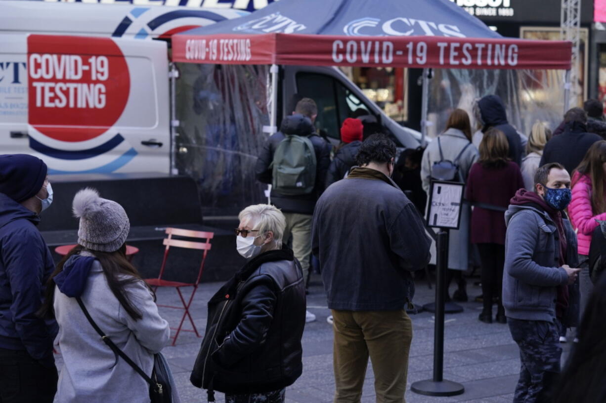 FILE - People wait in line at a COVID-19 testing site in Times Square, New York, Dec. 13, 2021. The new omicron coronavirus mutant speeding around the world may bring another wave of chaos, threatening to further stretch hospital workers already struggling with a surge of delta cases and upend holiday plans for the second year in a row.