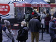 FILE - People wait in line at a COVID-19 testing site in Times Square, New York, Dec. 13, 2021. The new omicron coronavirus mutant speeding around the world may bring another wave of chaos, threatening to further stretch hospital workers already struggling with a surge of delta cases and upend holiday plans for the second year in a row.