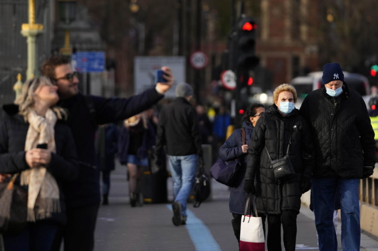 People walk across Westminster Bridge in London, Thursday, Dec. 9, 2021. British Prime Minister Boris Johnson has announced tighter restrictions to stem the spread of the omicron variant. He is again urging people to work from home and mandating COVID-19 passes to get into nightclubs and large events.