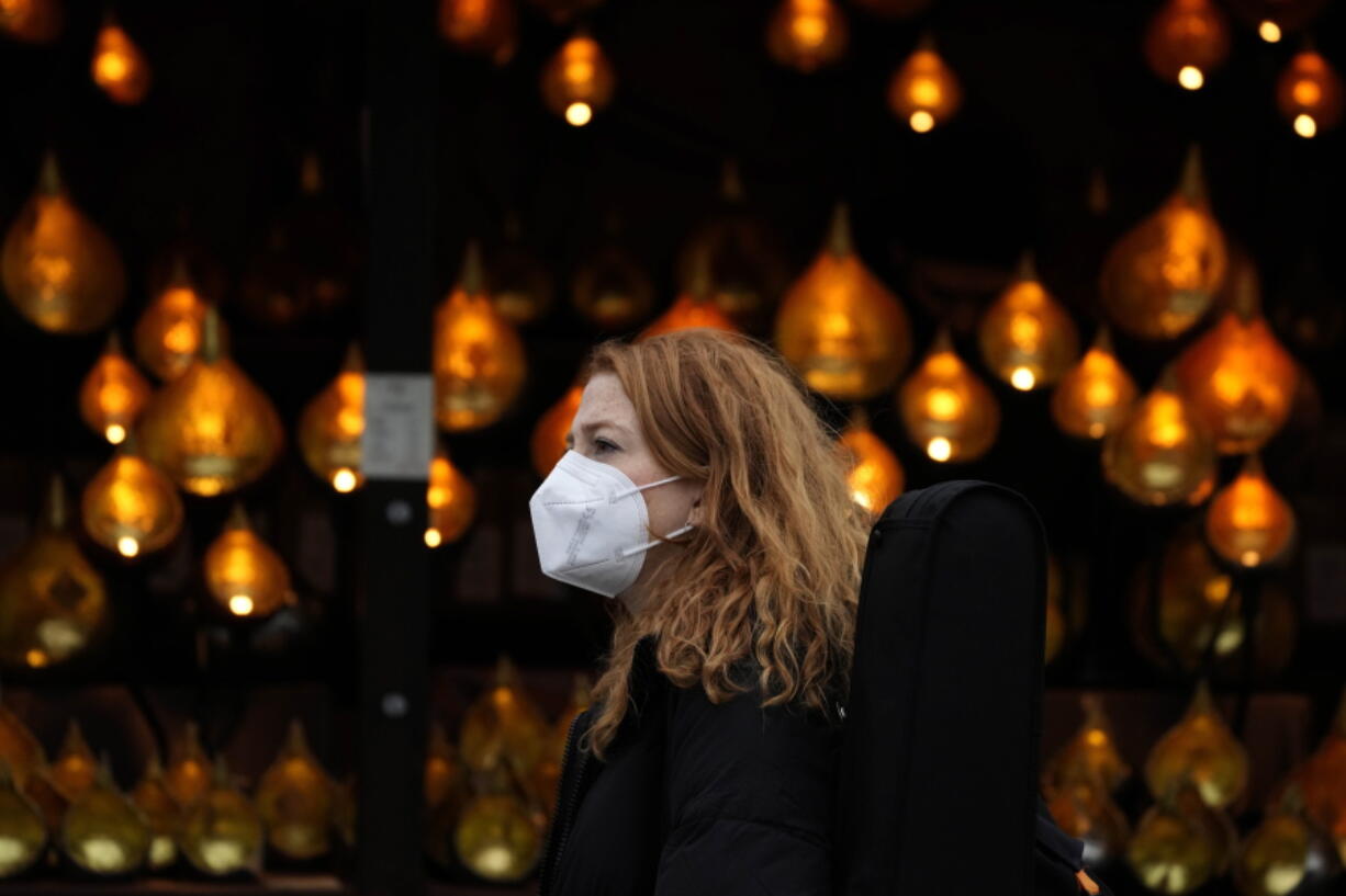 A woman wears a face covering as she passes a Christmas lights, in London, Wednesday, Dec. 22, 2021. British Prime Minister Boris Johnson said on Monday that his government reserves the "possibility of taking further action" to protect public health as Omicron spreads across the country.