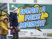 People walk past a billboard inviting citizens to wear face masks to curb the spread of COVID-19, in Nottingham, England, Monday Dec. 20, 2021. Britain's health secretary has refused to rule out imposing tougher COVID-19 restrictions before Christmas amid the rapid rise of infections and continuing uncertainty about the omicron variant.