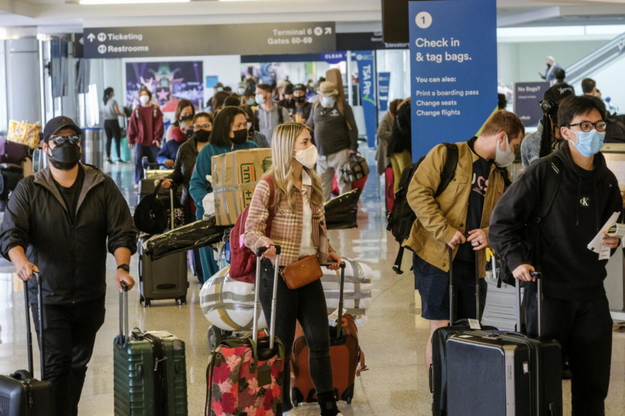 Holiday travelers wearing face masks line to check in at the Los Angeles International Airport in Los Angeles, Wednesday, Dec. 22, 2021. (AP Photo/Ringo H.W.