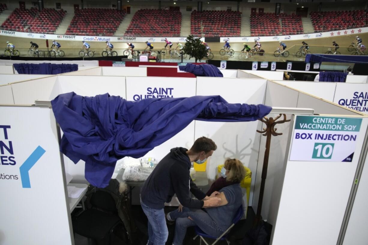 A woman receives Moderna COVID-19 vaccine as riders train at the National Velodrome in Saint-Quentin-en-Yvelines, west of Paris, France, Friday, Dec. 17, 2021. The government is holding a special virus security meeting Friday to address growing pressure on hospitals in France from rising infections.