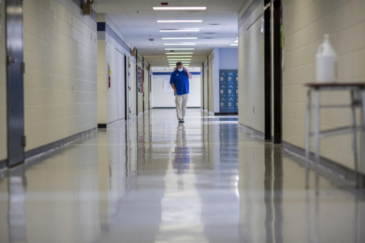 FILE - A middle school principal walks the empty halls of his school as he speaks with one of his teachers to get an update on her COVID-19 symptoms, Friday, Aug., 20, 2021, in Wrightsville, Ga. On Monday, Dec. 27, 2021, U.S. health officials cut isolation restrictions for Americans who catch the coronavirus from 10 to five days, and also shortened the time that close contacts need to quarantine. (AP Photo/Stephen B.