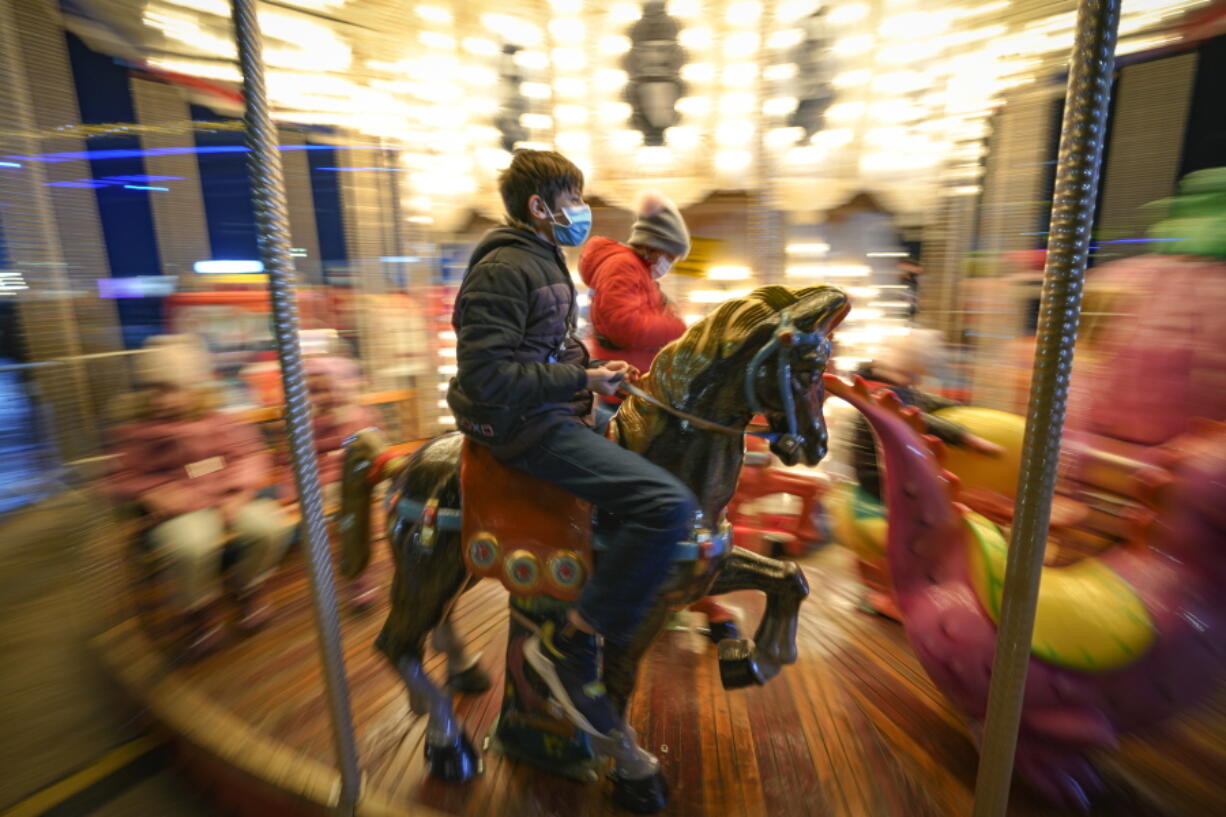 Children, some wearing face masks, enjoy a carousel ride at a Christmas fair in Bucharest, Romania, Saturday, Nov. 27, 2021. The Romanian capital will have three Christmas fairs open for public in the coming weeks and access to the venues will be conditioned by a COVID-19 green pas, proving the holder's vaccination or recovery after the infection.