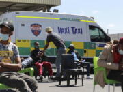 People wait to be vaccinated by a member of the Western Cape Metro EMS (Emergency Medical Services) at a mobile "Vaxi Taxi" which is an ambulance converted into a mobile COVID-19 vaccination site in Blackheath in Cape Town, South Africa, Tuesday, Dec. 14, 2021. The omicron variant appears to cause less severe disease than previous versions of the coronavirus, and the Pfizer vaccine seems to offer less defense against infection from it but still good protection from hospitalization, according to an analysis of data from South Africa, where the new variant is driving a surge in infections.