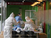 Medical workers wearing protective gear prepare to take samples at a temporary screening clinic for the coronavirus in Seoul, South Korea, Wednesday, Dec. 29, 2021.