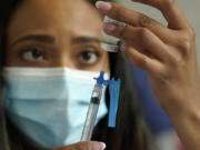 FILE - Licensed practical nurse Yokasta Castro, of Warwick, R.I., draws a Moderna COVID-19 vaccine into a syringe at a mass vaccination clinic, May 19, 2021, at Gillette Stadium, in Foxborough, Mass. While all eyes are on the new and little-understood omicron variant, the delta form of the coronavirus isn't finished wreaking havoc in the U.S. There is much that is unknown about omicron, including whether it is more contagious than previous versions, makes people sicker or more easily thwarts the vaccine or breaks through the immunity that people get from a bout of COVID-19.