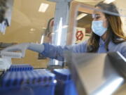 FILE - Kristin Grant, a microbiologist on the COVID-19 team at the Washington State Department of Health's Public Health Laboratory, loads samples that tested positive for COVID-19 into a machine that prepares them for automated genome sequencing, Tuesday, Dec. 7, 2021, in Shoreline, Wash. Data from the sequencing can then help determine which variant of the virus is present. (AP Photo/Ted S.