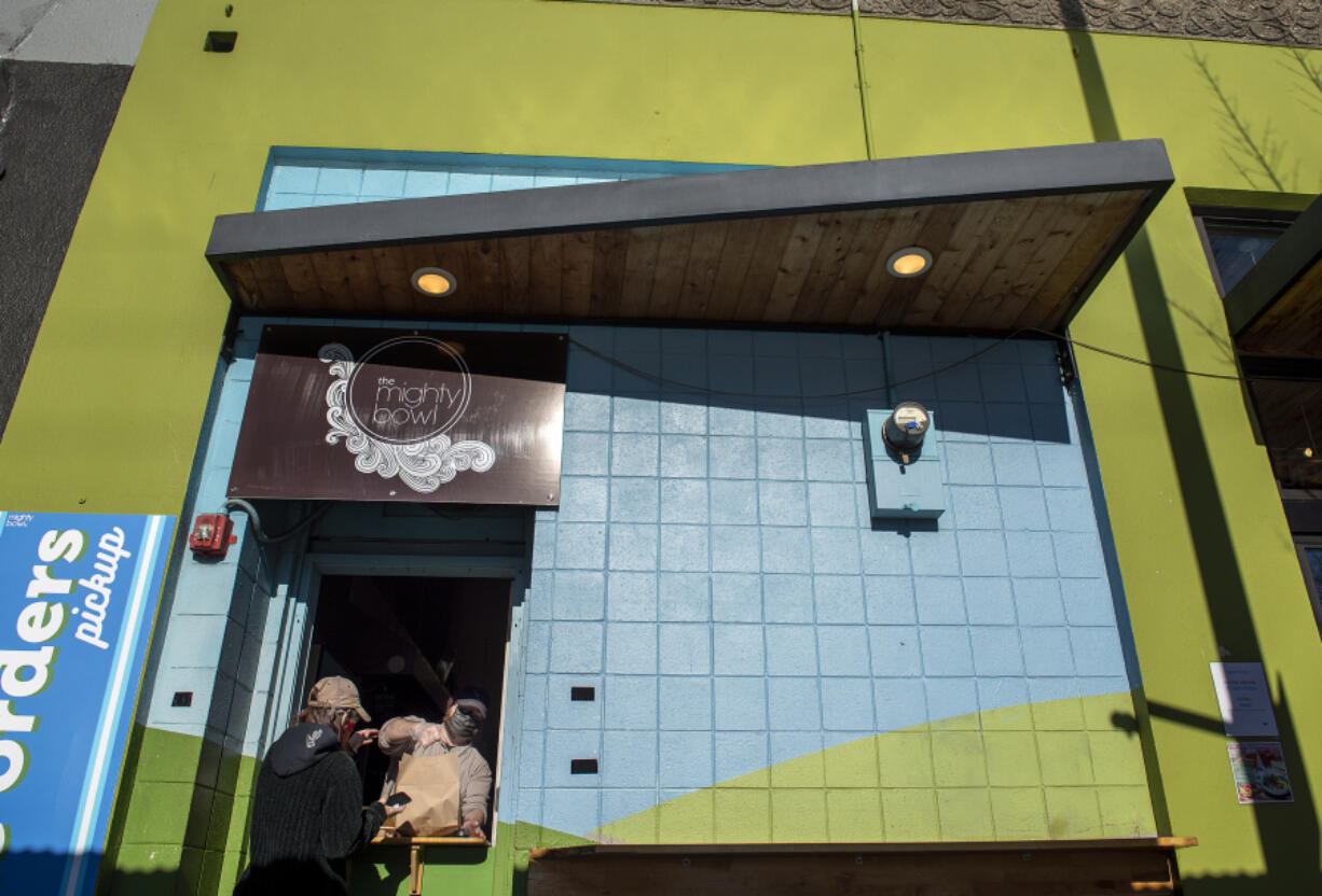 Vancouver resident Rose Wallace, left, picks up a takeout order from Louis Hodge at Mighty Bowl in downtown Vancouver. Restaurants around the state are struggling with supply chain issues, increased costs, omicron keeping customers away and omicron getting staff sick.