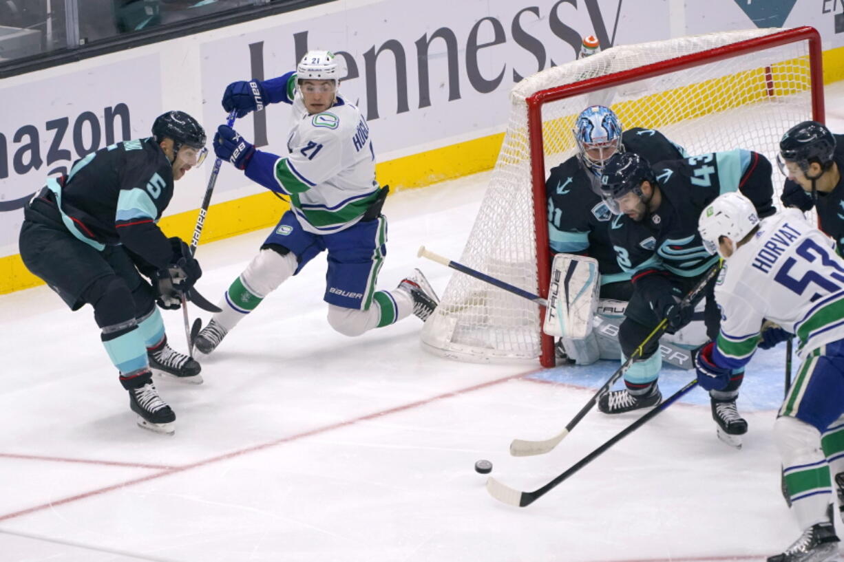 Vancouver Canucks left wing Nils Hoglander (21) passes the puck to center Bo Horvat (53) as Seattle Kraken center Colin Blackwell (43) defends in front of goaltender Philipp Grubauer during the first period of an NHL hockey game, Saturday, Jan. 1, 2022, in Seattle. (AP Photo/Ted S.