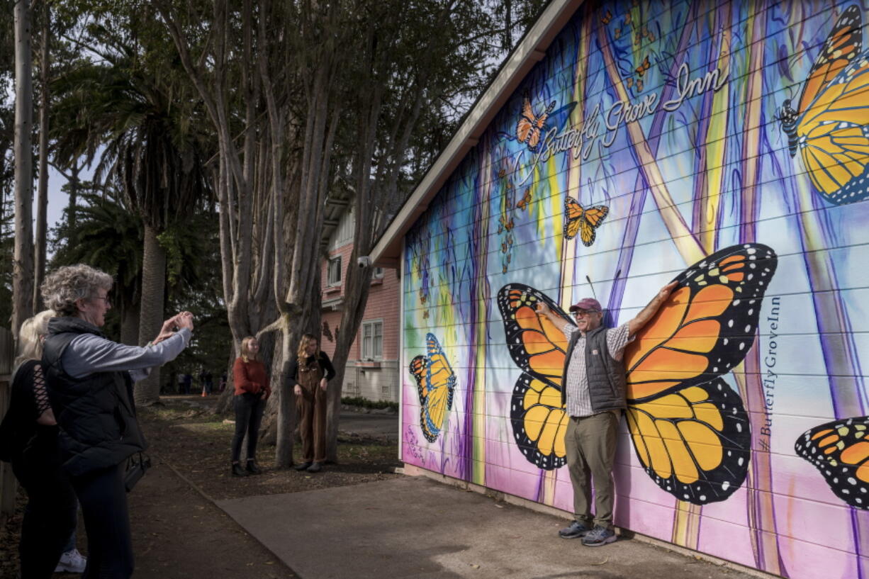 FILE - Leslee Russell of Livermore, Calif. takes a picture of her husband Dave Russell in front of a mural outside the Butterfly Grove Inn near the Monarch Grove Sanctuary in Pacific Grove, Calif., on Nov. 10, 2021. The number of Western monarch butterflies overwintering in California rebounded to more than 247,000 a year after fewer than 2,000 appeared, but the tally remained far below the millions that were seen in the 1980s, leaders of an annual count said Tuesday, Jan. 25, 2022.