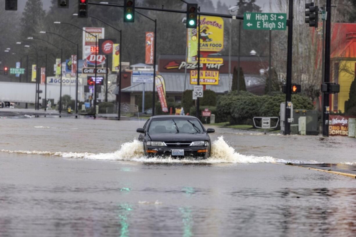 After driving past road closed signs a driver flows their way down Harrison Avenue Friday, Jan. 7, 2022, in downtown Centralia, Wash. The area is being flooded by the Skookumchuck River.