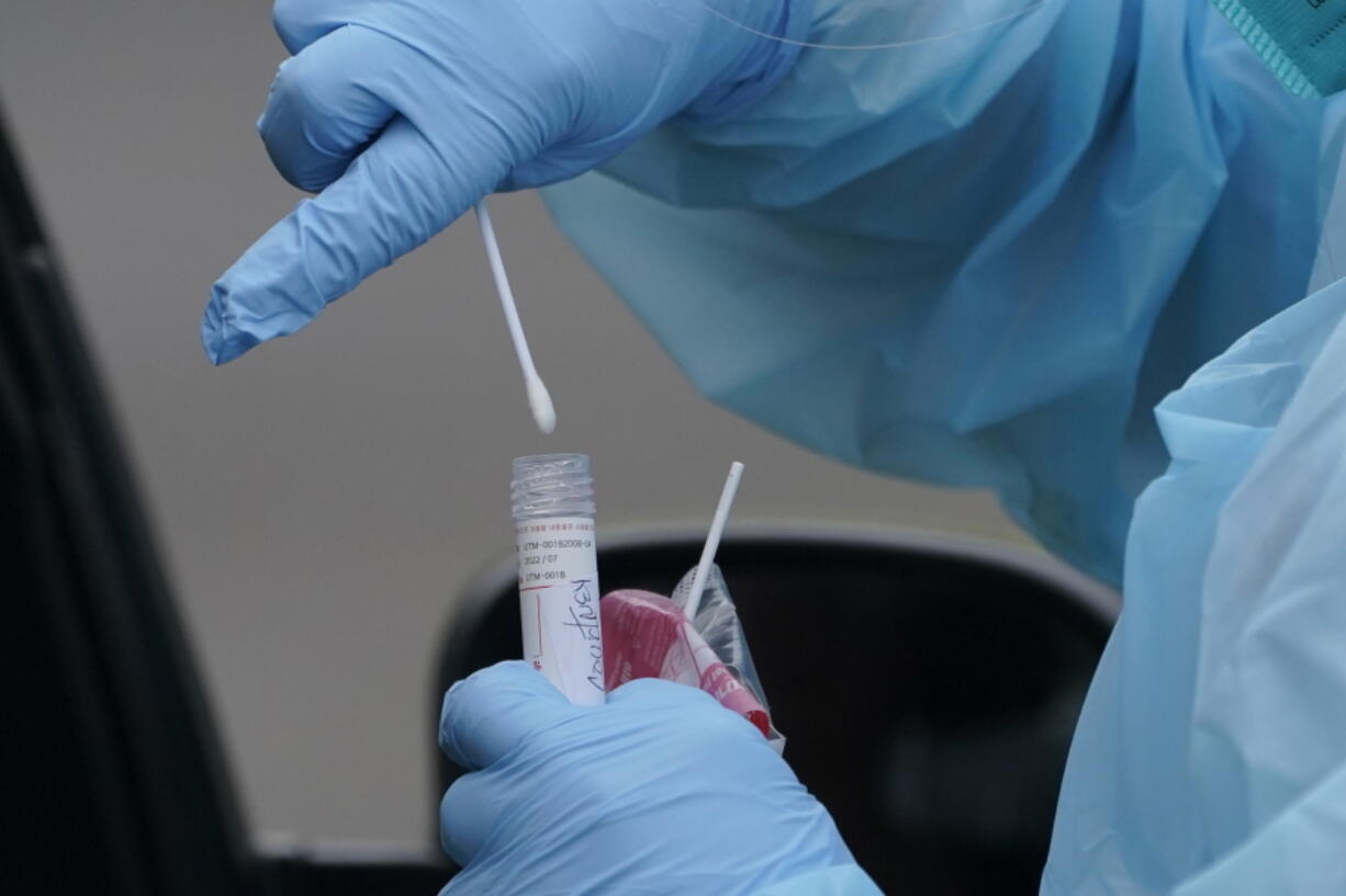 A worker at a drive-up COVID-19 testing clinic in Puyallup puts a nose swab into a tube of liquid. People who think they may have COVID-19 are urged to visit testing sites, not emergency rooms, to get a test. (Ted S.