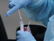 A worker at a drive-up COVID-19 testing clinic in Puyallup puts a nose swab into a tube of liquid. People who think they may have COVID-19 are urged to visit testing sites, not emergency rooms, to get a test. (Ted S.