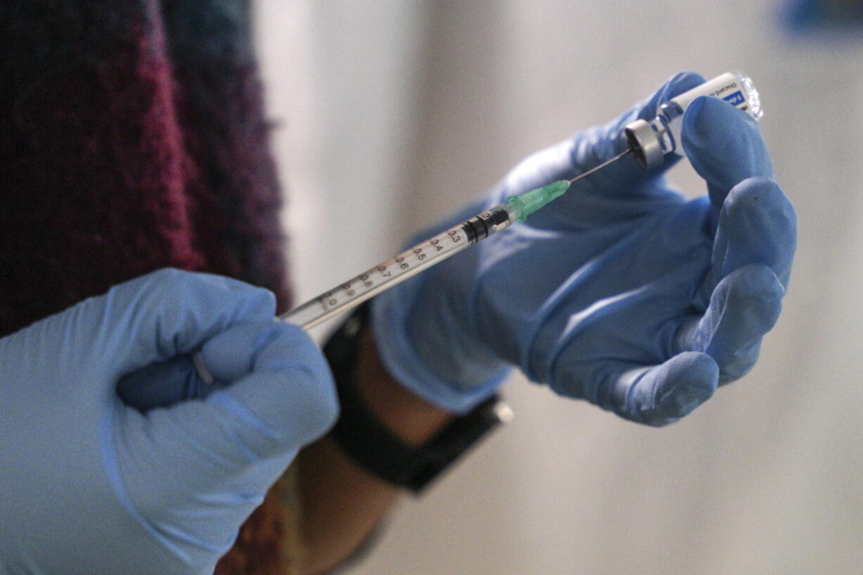 FILE - A staff member from the National Health Organisation (EODY) prepares a booster Johnson and Johnson vaccine against COVID-19 at Karatepe refugee camp, on the northeastern Aegean island of Lesbos, Greece, Wednesday, Dec. 15, 2021.  The fast-moving omicron variant is complicating a key question: How does the COVID-19 pandemic end and the world co-exist with this virus? Experts agree that the coronavirus is here to stay. Ending the pandemic won't be like flipping a light switch.