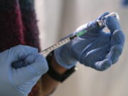 FILE - A staff member from the National Health Organisation (EODY) prepares a booster Johnson and Johnson vaccine against COVID-19 at Karatepe refugee camp, on the northeastern Aegean island of Lesbos, Greece, Wednesday, Dec. 15, 2021.  The fast-moving omicron variant is complicating a key question: How does the COVID-19 pandemic end and the world co-exist with this virus? Experts agree that the coronavirus is here to stay. Ending the pandemic won't be like flipping a light switch.