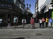 Wearing masks to curb the spread of the new coronavirus, people wait for a traffic light to change before crossing a street in San Jose, Costa Rica, Tuesday, Jan. 18, 2022.