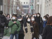 People wearing face masks to protect against the coronavirus walk on a street Wednesday, Jan. 26, 2022.