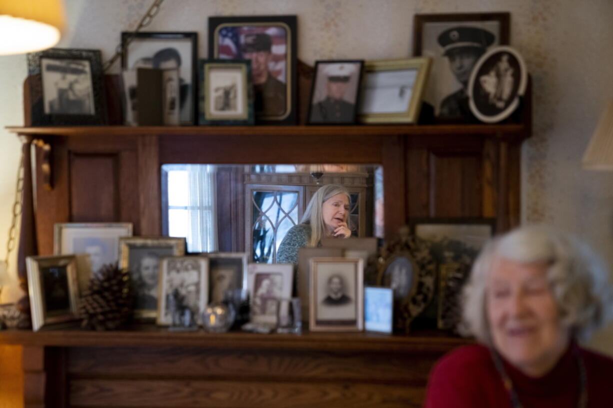 Nancy Rose, center in mirror, speaks with her mother, Amy Russell, right, who both contracted COVID-19 in 2021, in their dining room surrounded by pictures of relatives and family, Tuesday, Jan. 25, 2022, in Port Jefferson, N.Y. More than a third of COVID-19 survivors by some estimates develop lingering problems.