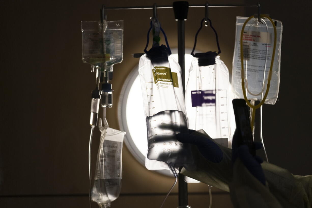 FILE - Nurse manager Edgar Ramirez checks on IV fluids while talking to a COVID-19 patient at Providence Holy Cross Medical Center in Los Angeles, Dec. 13, 2021. Some conservatives are taking aim at policies that allow doctors to consider race as a risk factor when allocating scarce COVID-19 treatments, saying the protocols discriminate against white people. Medical experts say the opposition is misleading. (AP Photo/Jae C.