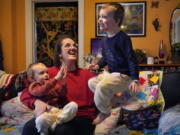 Heather Cimellaro holds her three-year-old son Charlie while his twin brother, Milo, jumps on a couch at their home, Wednesday, Jan. 5, 2022, in Auburn, Maine. Heather Cimellaro is one many parents concerned about the omicron surge and the dilemma it's posing for families of children too young to be vaccinated. (AP Photo/Robert F.