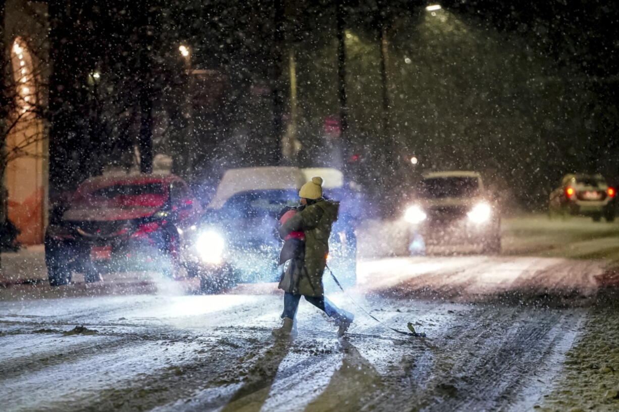 A person carries their dog as they cross Butler Street as snow falls during a winter storm that will impact the region on Sunday night, Jan. 16, 2022, in Lawrenceville a neighborhood in Pittsburgh.