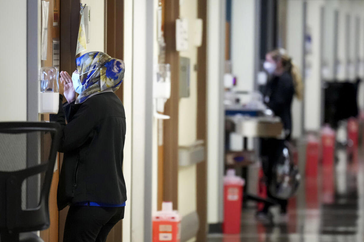 Nurses Fara Ajani, associate manager in medical services, peeks through the window of a patient room while making rounds in the COVID-19 unit at Parkland Hospital on Wednesday, Jan. 5, 2022, in Dallas. (Smiley N.