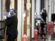 Nurses Fara Ajani, associate manager in medical services, peeks through the window of a patient room while making rounds in the COVID-19 unit at Parkland Hospital on Wednesday, Jan. 5, 2022, in Dallas. (Smiley N.