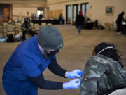 Jordan Bates of Aristo Healthcare, left, administers a dose of COVID-19 vaccine to a person experiencing homelessness at St. Joseph Catholic Church on Thursday. The clinic was part of the Washington State Department of Health's "Health-in-motion Care-a-van", which is a mobile vaccine clinic that made two stops in Vancouver.