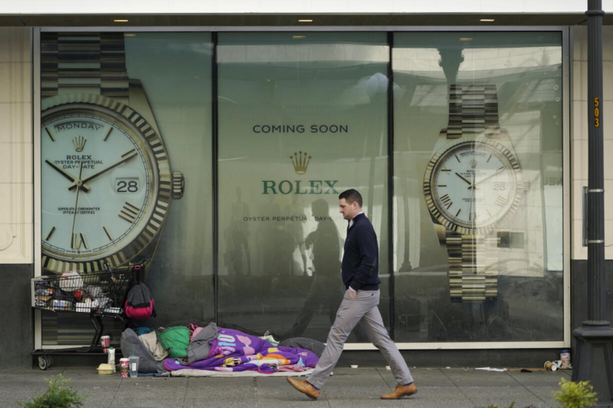 A person sleeps next to a shopping cart as a pedestrian walks past a store window advertising the future opening of a Rolex watch store on Jan. 31 in downtown Seattle. (ted s.