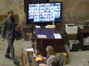 With most Senators attending remotely and shown on a video display, legislative workers are shown on the Senate floor, Wednesday, Jan. 26, 2022, at the Capitol in Olympia, Wash., during debate on a measure that would delay implementation of a long-term care program and the payroll tax that pays for it. The Senate passed the measure, which was passed by the House last week, and Gov. Jay Inslee is expected to sign the measure on Friday. (AP Photo/Ted S.