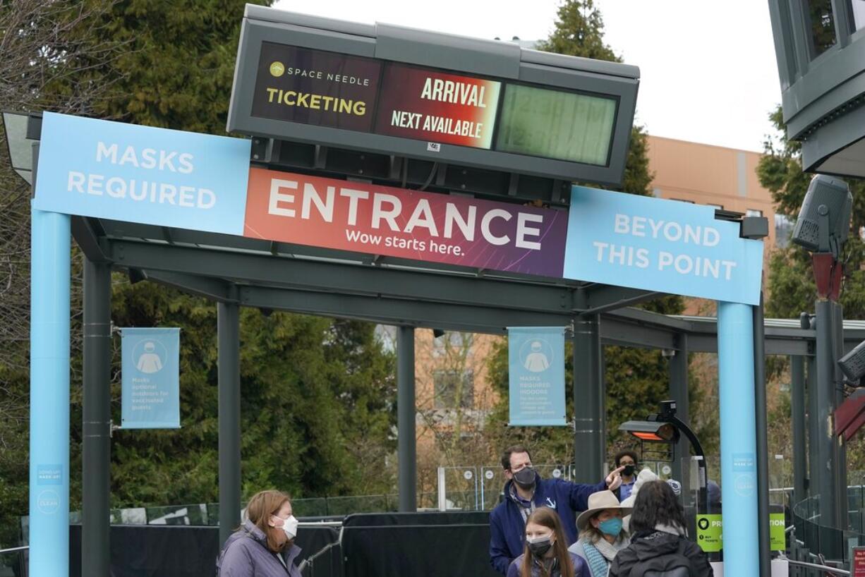 A worker talks to guests arriving at the Space Needle under a sign that reads "Masks Required," Thursday, Feb. 17, 2022, in Seattle. Gov. Jay Inslee said Thursday that the statewide indoor mask mandate in Washington state will lift on March 21, 2022, including at schools and child care facilities. (AP Photo/Ted S.