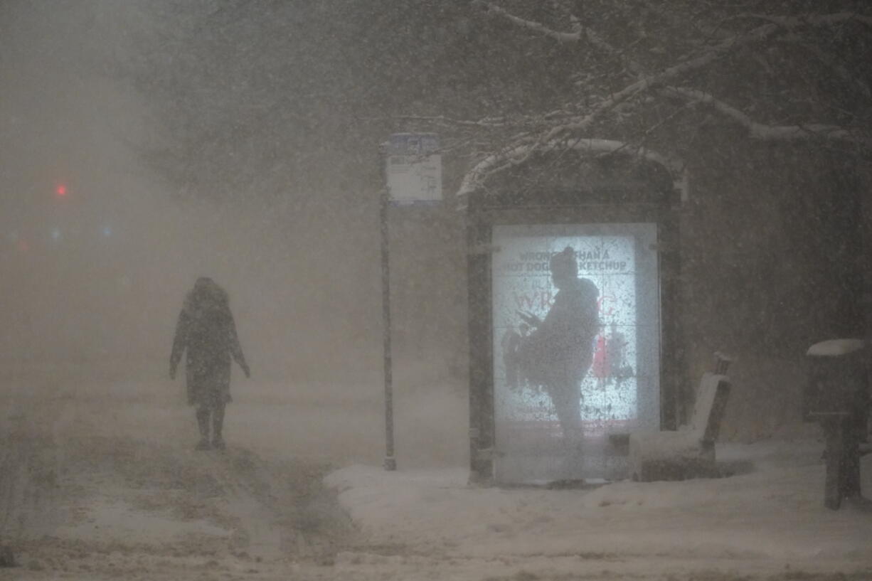 A woman walks to a bus shelter on Dr. Martin Luther King Drive as a man waits in the shelter during the pre-dawn hours Wednesday, Feb. 2, 2022, in Chicago.  A major winter storm with millions of Americans in its path brought a mix of rain, freezing rain and snow to the middle section of the United States as airlines canceled hundreds of flights, governors urged residents to stay off roads and schools closed campuses.