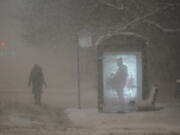 A woman walks to a bus shelter on Dr. Martin Luther King Drive as a man waits in the shelter during the pre-dawn hours Wednesday, Feb. 2, 2022, in Chicago.  A major winter storm with millions of Americans in its path brought a mix of rain, freezing rain and snow to the middle section of the United States as airlines canceled hundreds of flights, governors urged residents to stay off roads and schools closed campuses.