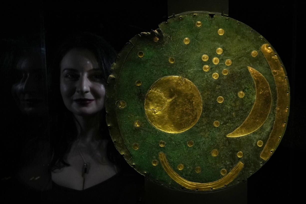 A staff member poses next to the Nebra Sky Disc, which dates from around 1600 BCE, and is the oldest surviving representation of the cosmos, on display at the "The World of Stonehenge" exhibit at the British Museum in London.