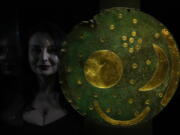 A staff member poses next to the Nebra Sky Disc, which dates from around 1600 BCE, and is the oldest surviving representation of the cosmos, on display at the "The World of Stonehenge" exhibit at the British Museum in London.