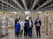 Gov. Gavin Newsom, right, walks through rows of boxed Personal protective equipment, PPE, with dignitaries and elected officials, as he prepares to announce the next phase of California's COVID-19 response called "SMARTER," during a press conference at the UPS Healthcare warehouse in Fontana, Calif., on Thursday, Feb. 17, 2022. The plan is to move from the pandemic stage into an endemic stage in which people will learn to live COVID.